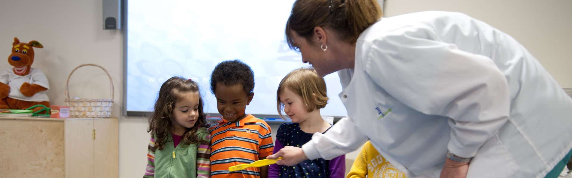 Female dentist showing three children yellow tooth brush